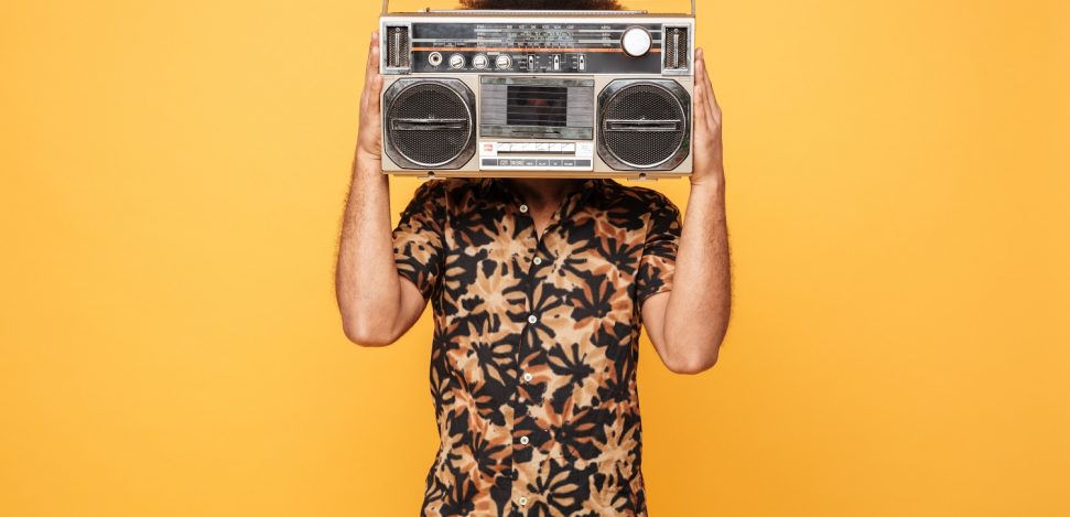 Image of young african man standing covering face with tape recorder isolated over yellow background.